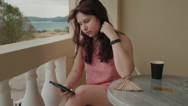 Young Woman Bright Dress Sitting Chair Hotel Balcony Holding Phone — Vídeo de Stock