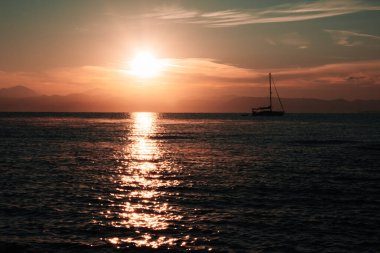 İlk Güneş ışınları deniz yüzeyini aydınlatıyor. Dağ sırasının silueti ve yatı. Yatlar heyecan verici maceralar, uzun deniz yolculukları, dalış ve arkadaşlarla rahatlama ile ilişkilidir.