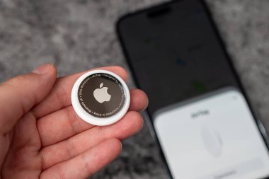 Jurmala, Letonya - 21 09 2023: Kadınların elinde küçük AirTag Apple, arka planda odaklı akıllı telefon cadısı etiketle bağlantılıdır. Eşyalarının izini sürmek için hava etiketi cihazı. Yüksek kalite fotoğraf