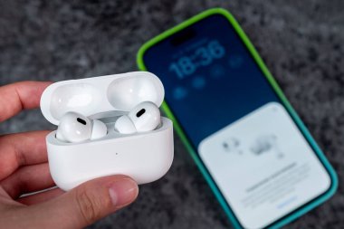 Jurmala, Letonya - 21 09 2023: Kadın elinde kulaklıklı bir çanta var - Airpod Pro 2 nesil. Arka planda akıllı telefon cadıları hava kapsüllerine bağlıdır. Yüksek kalite fotoğraf