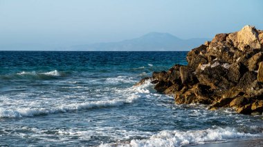 Mesmerizing landscape with the sea in which waves rage and crash against stone breakwaters, with mountains visible in the distance. . High quality photo clipart