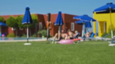 Güneş pansiyonlarında güneşlenen ve güneş şemsiyeleri altında bungalovların arka planında güneşlenen insanların bulanık zaman aralıkları. Yüksek kalite 4k görüntü