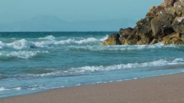 Okyanus sakin ve dalgalar küçük. Kumsal kayalık ve su mavi.