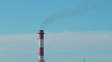 İçinden duman çıkan uzun kırmızı ve beyaz bir kule. Gökyüzü mavi ve hiç bulut yok.