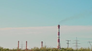 İçinden duman çıkan kırmızı ve beyaz bir enerji santrali. Gökyüzü mavi ve hiç bulut yok.