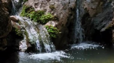 İçinden su akan bir şelale. Su berrak ve kayalar yeşil.