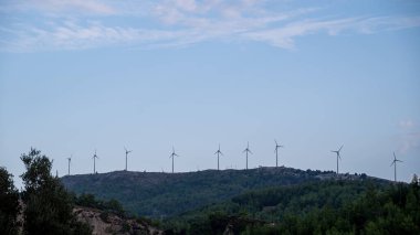 Tepenin yamacında bir sıra rüzgar türbini var. Gökyüzü mavi ve arka planda bulutlar var. Yüksek kalite fotoğraf
