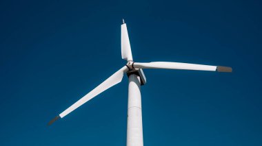 Bir rüzgar türbini gökyüzünde dimdik duruyor. Gökyüzü mavi ve berrak ve görünen tek şey rüzgar türbini.