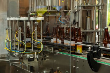 Riga, Letonya - 09 09 09 2023: Karmaşık bir makine hızla hareket eden bir fabrika ortamında hızlı bir taşıma bandındaki bira şişelerini verimli bir şekilde dolduruyor
