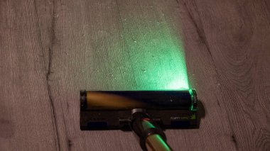  Jurmala, Letonya 08.07.2024: Üzerinde parlak yeşil ışık parlayan bir elektrik süpürgesi, odadaki güzel cilalanmış ahşap zemini özenle temizliyor