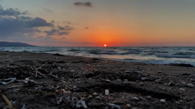Güneş okyanusun üzerinde batıyor, plajın üzerine sıcak bir parıltı saçıyor. Su sakin ve gökyüzü turuncu ve pembe renklerin karışımı.