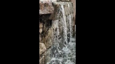 Su zarif bir şekilde taştan bir yapının üzerinden akar ve huzurlu bir açık havada rahatlatıcı bir atmosfer yaratır. Öğleden sonra ışığı rahatlatıcı sahneyi güçlendirir..