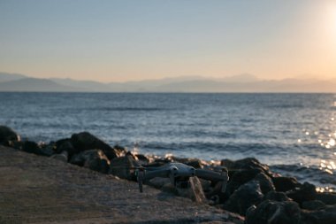 Bir dron kayalık bir kıyıya yakın okyanusun üzerinde uçuyor. Gökyüzü mavi ve su sakin.
