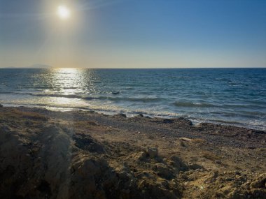 Güneş okyanusun üzerinde batıyor, suya altın ışık saçıyor ve sahili aydınlatıyor. Dalgalar yavaşça kıyıya vurur ve sakin bir atmosfer yaratır..