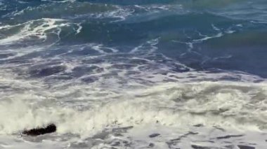 Güneş ufukta batarken dalgalar yavaşça kayalara çarpıyor. Suyun sakinleştirici sesi bu güzel sahil bölgesinde sakin bir atmosfer yaratıyor..