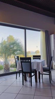 Parlak bir yemek alanında, sandalyelerle çevrili bir masada sakin bir sabah boyunca palmiye ağaçları ve uzak dağların çarpıcı manzarası sergilenir..
