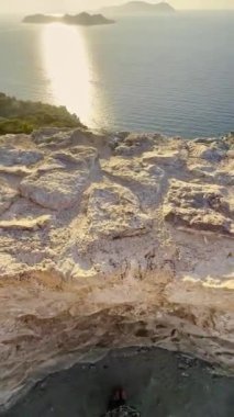 Gün batımı, sakin okyanus sularına kayalık bir tepeden altın bir ışık saçar. Uzak adalar, barışçıl atmosferi geliştirmek için pitoresk bir zemin oluşturur..