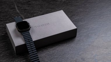 Jurmala, Letonya 11.01.2025: New Apple Watch Ultra 2 Black Titanium. Modern bir akıllı kol, zarif bir şekilde tasarlanmış ambalajının yanındaki koyu ahşap bir yüzeye dayanır. Şık kayış, zarafeti tamamlıyor.