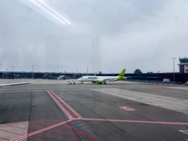 Riga, Letonya - 01.10.2024: Terminalde bir havayolu uçağı duruyor, bulutlar arka planda yoğun havaalanının üzerinde gezinirken, verimli bir seyahat ortamı sergiliyor.