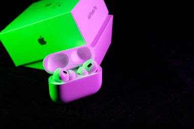 Jurmala, Letonya - 01.05.2025: Apple Kulaklıklar - Airpod Pro 2. Kablosuz kulaklıklar açık ve şarj çantasında duruyor, yeşil ışıkla aydınlatılıyor.. 