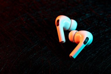 Jurmala, Letonya - 01.05.2025: Apple Kulaklıklar - Airpod Pro 2. Kablosuz kulaklıklar, parlak kırmızı ve mavi ışıklı koyu renkli bir yüzeye yerleştirilmiştir. Odak, zarif tasarımlarını gözler önüne seriyor..