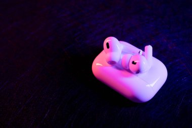 Jurmala, Letonya - 01.05.2025: Apple Kulaklıklar - Airpod Pro 2. Kablosuz kulaklıklar şarj çantalarına yerleştirilir, koyu bir ortamda canlı mor ve mavi ışıklar altında parlarlar..