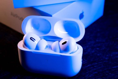 Jurmala, Letonya - 01.05.2025: Apple Kulaklıklar - Airpod Pro 2. Zarif bir şarj çantası, yumuşak mavi ışıkla aydınlatılan kablosuz kulaklıklar taşır. Sahne, modern teknolojiyi karanlığa karşı sergiliyor.