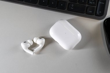 Jurmala, Letonya - 01.05.2025: Apple Kulaklıklar - Airpod Pro 2. Kablosuz kulaklıklar, temiz bir masanın üzerindeki şarj çantasının yanında duruyor. Yakınlarda bir bilgisayar klavyesi var ve bir minimalist yaratıyor.