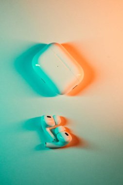 Jurmala, Letonya - 01.05.2025: Apple Kulaklıklar - Airpod Pro 2. Kablosuz kulaklıklar ve şarj çantası, mavi ve turuncu renklerin yumuşak eğimli arka planında belirgin bir şekilde gösterilir..