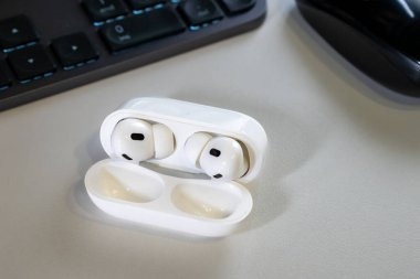Jurmala, Letonya - 01.05.2025: Apple Kulaklıklar - Airpod Pro 2. Kablosuz kulaklıklar şarj masasında duruyor. Yakınlarda, bir bilgisayar klavyesi ve bir bilgisayar faresi görülebilir.