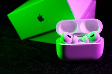 Jurmala, Letonya - 01.05.2025: Apple Kulaklıklar - Airpod Pro 2. Kablosuz kulaklıklar şarj kabinlerinde duruyor, canlı neon renklerle aydınlatılıyor, ambalajın yanında modern bir atmosfer yaratıyor..