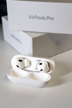 Jurmala, Letonya - 01.05.2025: Apple Kulaklıklar - kutulu Airpod Pro 2. Kablosuz kulaklıklar şarj çantasının içinde temiz bir yüzeyde duruyor. Arka planda bir ürün kutusu görünür.