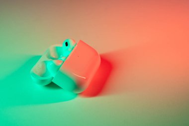 Jurmala, Letonya - 01.05.2025: Apple Kulaklıklar - Airpod Pro 2. Kablosuz kulaklıklar, yeşil ve kırmızı ışıklarla hafifçe aydınlatılan pürüzsüz bir yüzeye yerleştirilir..