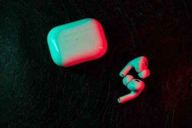 Jurmala, Latvia - 01.05.2025: Apple Headphones - AirPods Pro 2. gen Close-up view of a charging case and wireless earphones placed on a dark surface, illuminated with bright, contrasting colors. Ideal