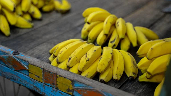 Meyve pazarında taze muz demetleri ahşap yüzeyde tutulur. Seçici odak.