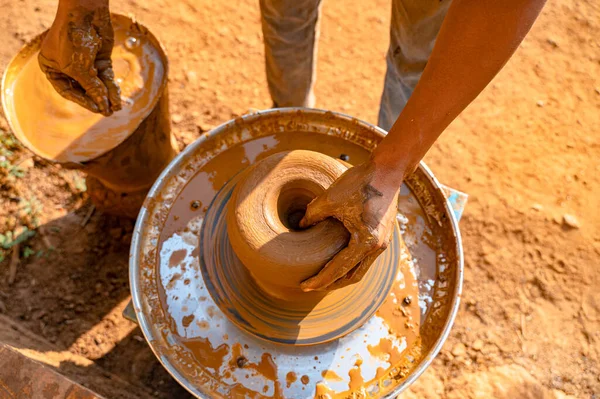 stock image Potter making clay pot by using hand on the electric pottery, giving shape to the pot and one hand near muddy water bucket to take water from it during morning light.