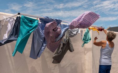 Langebaan, Güney Afrika. 2023. Rüzgarlı bir günde arka bahçesinde çamaşırları asan yaşlı bir kadın..