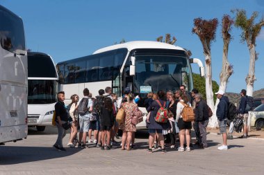 Elounda, Girit, Yunanistan. 2023. Gezginler tur otobüslerine binmek için Girit 'te popüler bir sahil şeridi olan Elounda' daki otobüs durağında bekliyorlar.