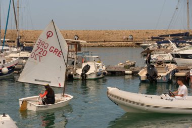 Heraklion, Girit, Yunanistan, Avrupa. 2023. Genç kız eski limandaki bir sandalda yelkenli dersinde limandaki Heraklion, Girit 'teki eğitmen tarafından izleniyor..