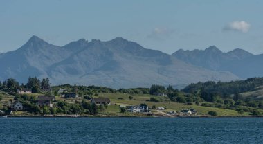 Isle of Skye, Scotland, UK. 6 June 2023. Panoramic view of the Cuillin mountains across green countryside and residential homes on the Isle of Skye. clipart