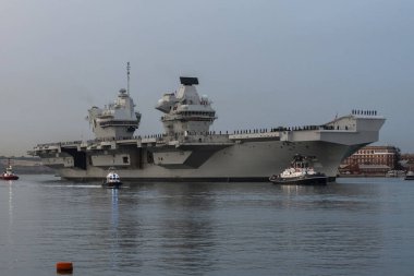 Portsmouth, İngiltere, İngiltere. 8 Eylül 2023. İngiliz donanma uçak gemisi hava kararınca Portsmouth tersanesinden kalkıyor. Römorkör ve güvenlik gemileriyle birlikte. Donanma personeli güverteleri doldursun.. 