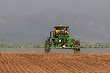 Batı Burnu, Güney Afrika. 24 Nisan 2024. Sprey kollu traktör, sondaj makinesi Batı Burnu 'ndaki tarım arazisine kanola tohumu ekmeden önce su püskürtüyor..