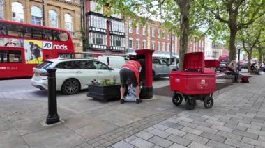 Salisbury Wiltshire İngiltere. 29.04.2024. Elinde çuval olan bir postacı Salisbury şehir merkezindeki kırmızı bir posta kutusundan mektuplar yollamış..