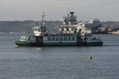 Portsmouth Harbour England UK. 20.06.2024. Gosport passenger ferry crossing Portsmouth harbour in background HMS Prince of Wales aircraft carrier. clipart