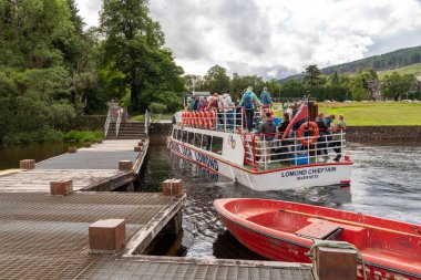 Tarbet Argyll ve Bute Scottland UK. 06.07.2025. Lomond Gölü 'nün batı kıyısındaki Tarbet' e yanaşan bir tekne ve yolcularla dolu iskele..