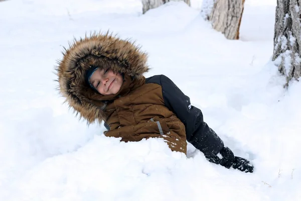 Active games in nature in winter. The boy is fooling around, buried in the snow. He looks at the camera and smiles.