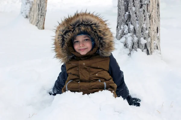 Active games in nature in winter. The boy is buried in the snow. He looks at the camera and smiles.