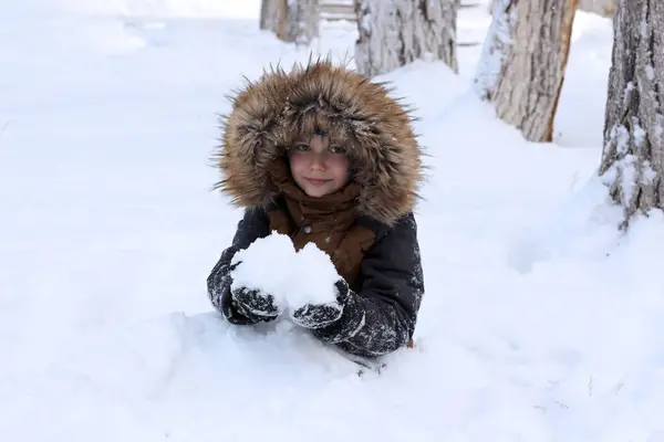 Active games in nature in winter. The boy is buried in a mountain of snow. He holds snow in his hands and looks at the camera.