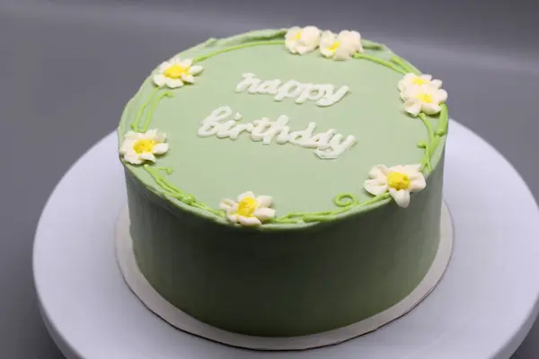 Green handmade cake with flowers and the inscription Happy Birthday on a gray background.
