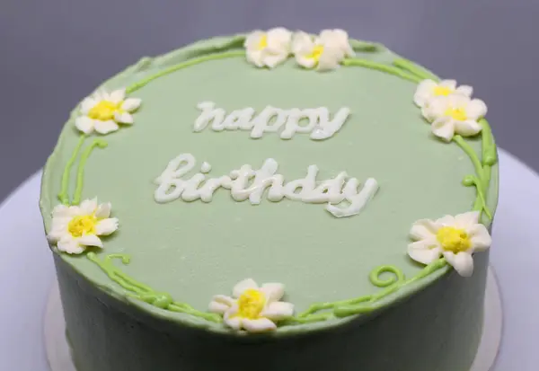 Green handmade cake with flowers and the inscription Happy Birthday on a gray background close up.